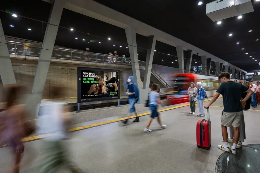 Digitale Großbildfläche an einem Bahnsteig zeigt das Kampagnenmotiv „Blöde Mathe kann auch die KI. Geile Matte kannst nur du.“